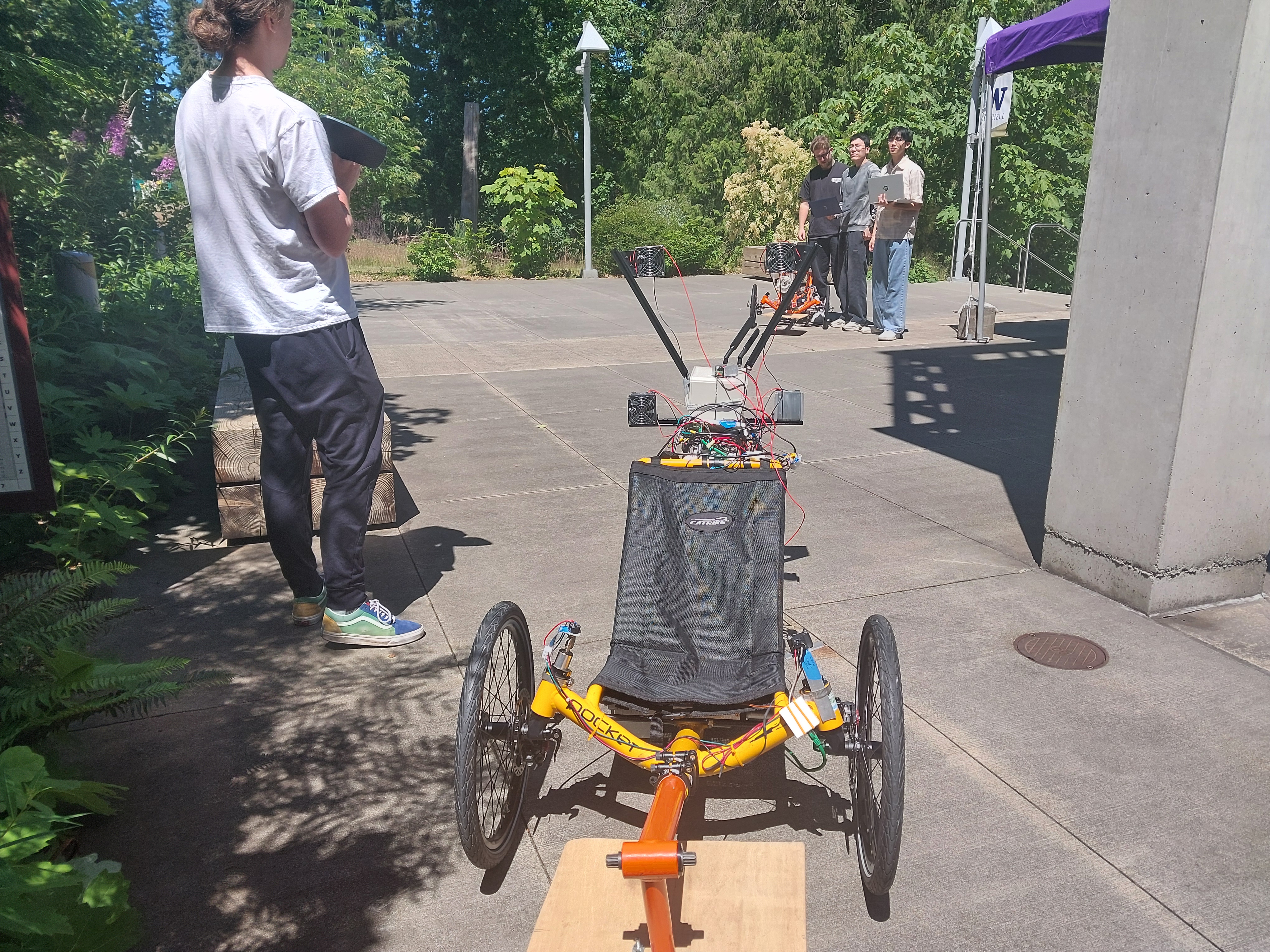 Four capstone students stand outside with laptops testing the sensors that measure distance between two autonomous trikes.